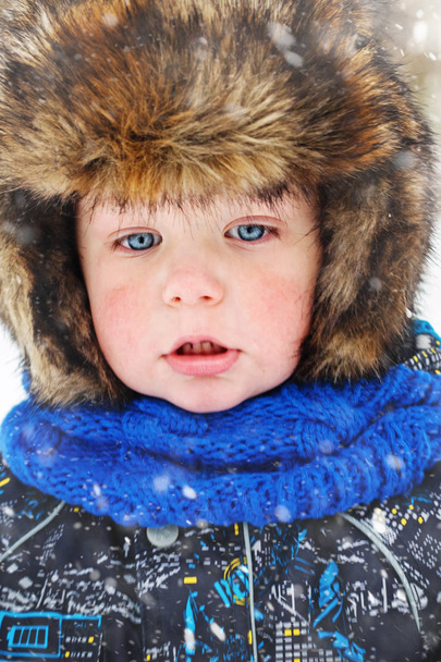 schönes niedliches Gesicht eines kleinen Jungen mit Wintermütze und Ohrenklappen. große Augen. Nahaufnahme. - Foto, Bild