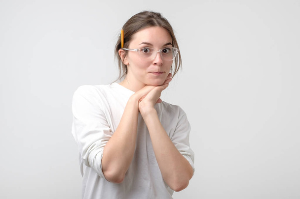 Думает любопытная молодая женщина в очках с карандашом возле уха, смотрящая в камеру
 - Фото, изображение