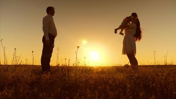 Μικρή κόρη πηγαίνει στη μητέρα της στην αγκαλιά της το ηλιοβασίλεμα. Ευτυχισμένη μητέρα αγκαλιές και φιλιά μωρό. Ο μπαμπάς, η μαμά και μωρό παίζουν για βόλτα το βράδυ. Πρώτα βήματα - Φωτογραφία, εικόνα