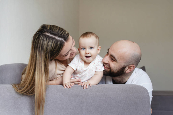 Smiling mother and father holding their baby girl daughter sitting on bed at home - Fotografie, Obrázek