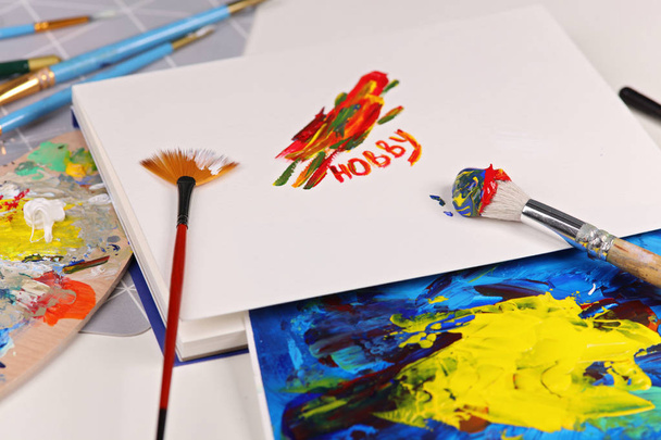 Hobby, malířství, umění, tvořivost koncept. Umělecké zařízení: kartáče, trubky barev, palety a malby na stole - Fotografie, Obrázek