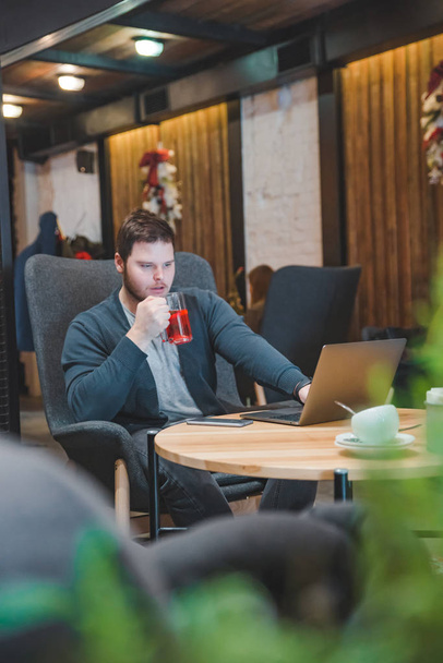 jonge volwassen man die op laptop in café werkt. vruchten thee drinken. freelance lifestyle - Foto, afbeelding