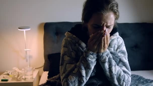 Young sick woman with fever sneezing at night in bed. Medicines, thermometer and glass of water on the table. - Materiaali, video