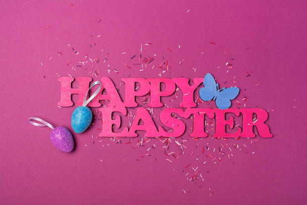 Draufsicht auf rosa Text von glücklichen Ostern und glitzernden Eiern mit bunten Zuckerstreuern oder Konfetti als Backdekor auf lila Hintergrund - Foto, Bild