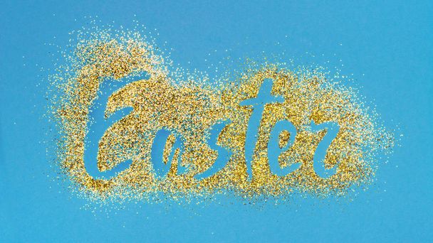 Top view on handwritten shiny text of easter made with golden glitter on blue background - Photo, image