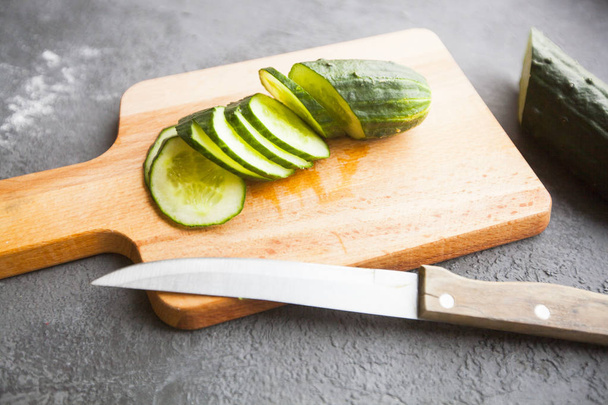 Heathy food Vegetarian Concept. Cutting a fresh cucumber on a wooden board, dark concrete background with copy space, top view - Foto, Imagem