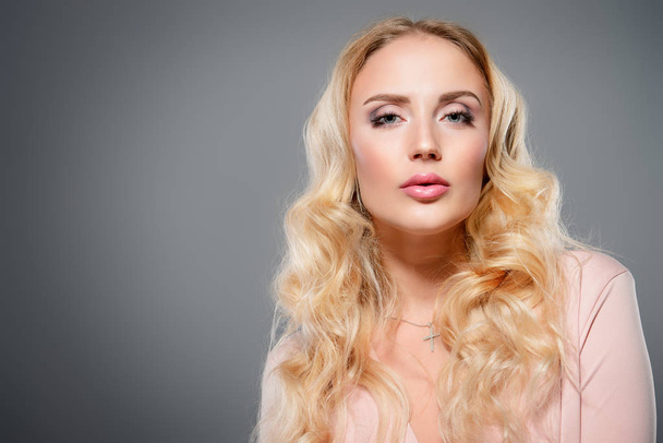 Portret van een mooie vrouw met blonde lange haren. Beauty, haarverzorging, cosmetica concept. Gezondheidszorg. Grijze achtergrond. - Foto, afbeelding
