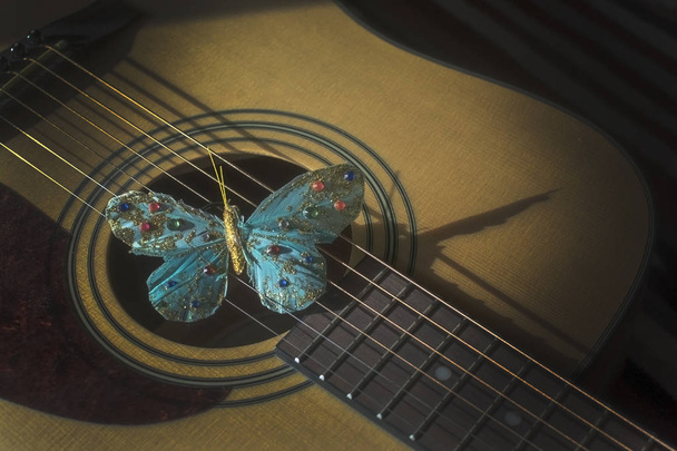 Бирюзовая бабочка на струнах акустической гитары, концепция поэзии, музыкальности, творчество певца-песенника. - Фото, изображение