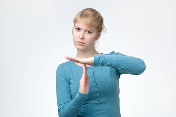 Beautiful woman in blue shirt showing time out sign over gray background - Photo, Image