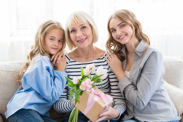 Generatie vrouwen. Oma met cadeautjes, moeder en dochter knuffelen grootmoeder - Foto, afbeelding
