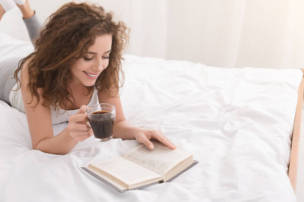 Allegro libro di lettura ragazza e bere caffè a letto
 - Foto, immagini