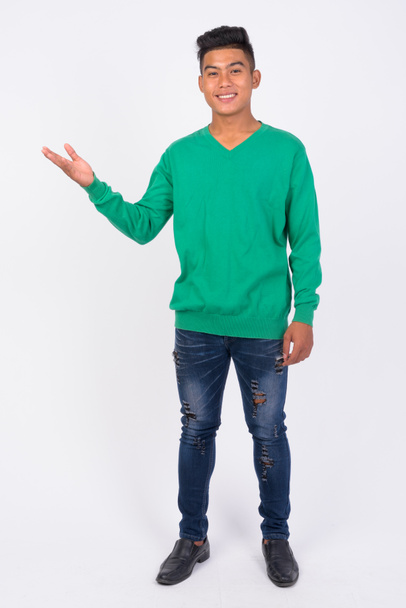 Full body shot of young happy Asian man showing something - Photo, image