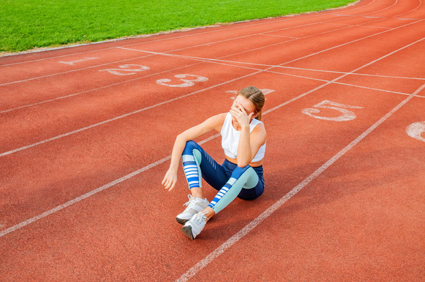 Tired woman runner taking a rest after run sitting on the running track - Фото, изображение