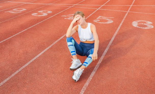 Tired woman runner taking a rest after run sitting on the running track - 写真・画像