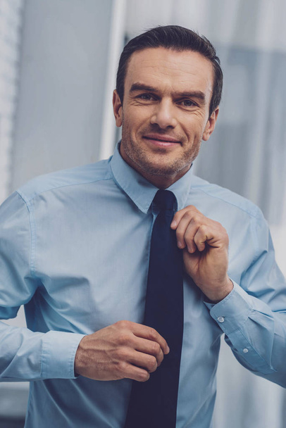 Joyful positive man holding his tie - Zdjęcie, obraz