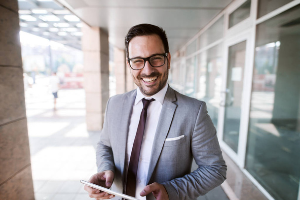 Primo piano di uomo d'affari sorridente in abbigliamento formale che tiene tablet mentre in piedi all'aperto
. - Foto, immagini