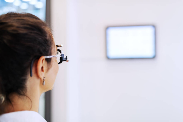 Donna che controlla la vista mentre guarda lo schermo sul muro dell'ottico
. - Foto, immagini