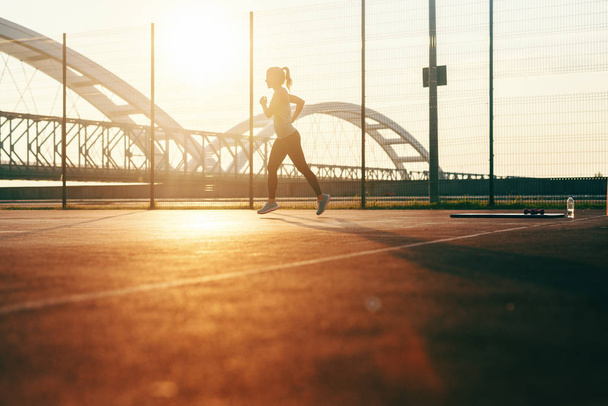Силуэт спортивной женщины, бегущей на корте рано утром в летнее время
. - Фото, изображение