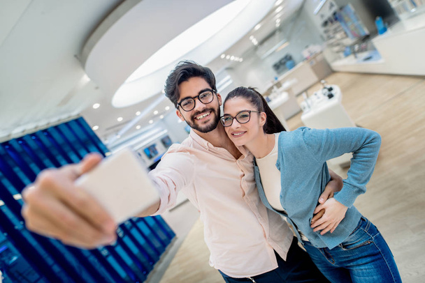 Młoda szczęśliwa para w elektronice przechowywać biorąc selfie - Zdjęcie, obraz