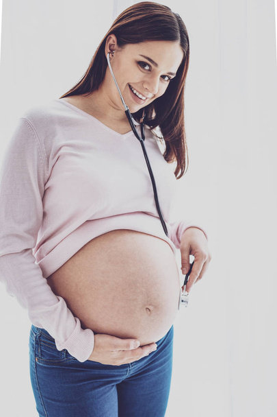 Pregnant woman using stethoscope to listen to baby in belly - Zdjęcie, obraz
