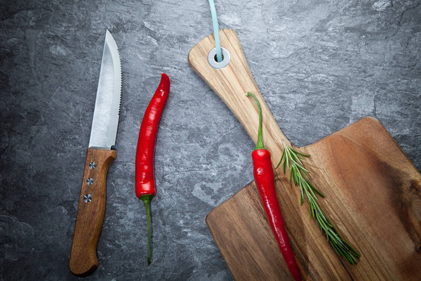 Red hot chilli peppers, rosemary, knife and wooden board on grey table - Foto, Bild
