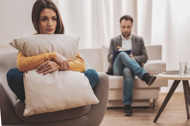 Stressed woman holding pillow while sitting in front of therapist - Foto, Imagem