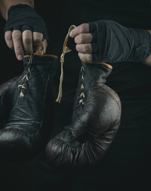 Bir çift çok eski boks eldiveni erkeklerin ellerinde siyah bir bandajla sarılmış. - Fotoğraf, Görsel