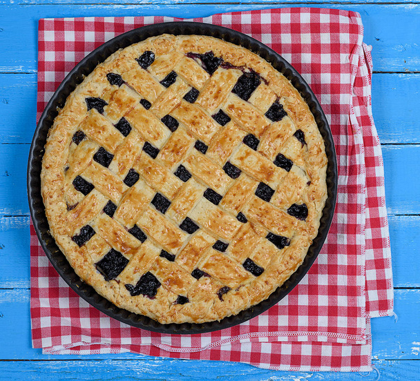 baked round black currant cake on an iron plate, top view, wooden blue background  - Φωτογραφία, εικόνα