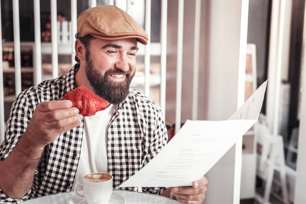 Man choosing items in the menu while eating the croissant - Fotografie, Obrázek
