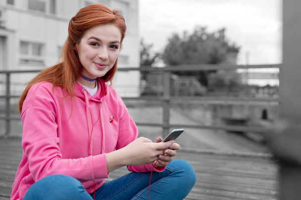 Young girl wearing pink pullover smiling and holding modern gadget - 写真・画像