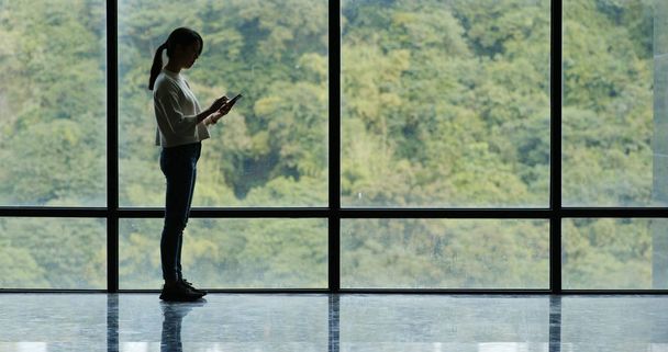 Kobieta przy użyciu telefonu komórkowego i chodzenie w oknie szkło - Zdjęcie, obraz