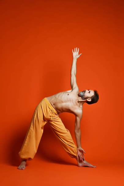 Fitness senior man doing exercise yoga asana leg isolated on a orange background - 写真・画像