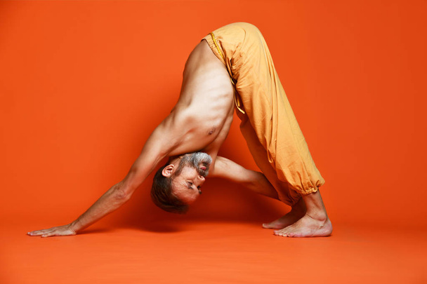 Old man practicing yoga doing stretching exercises against orange background - Photo, image