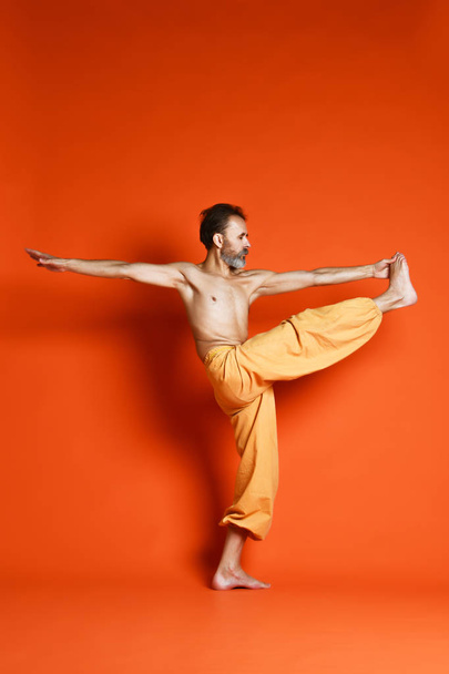 Old man practicing yoga doing stretching exercises against orange background - Foto, Imagem