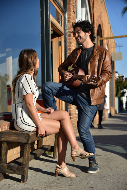 Handsome young man serenading an attractive woman outdoors - 写真・画像