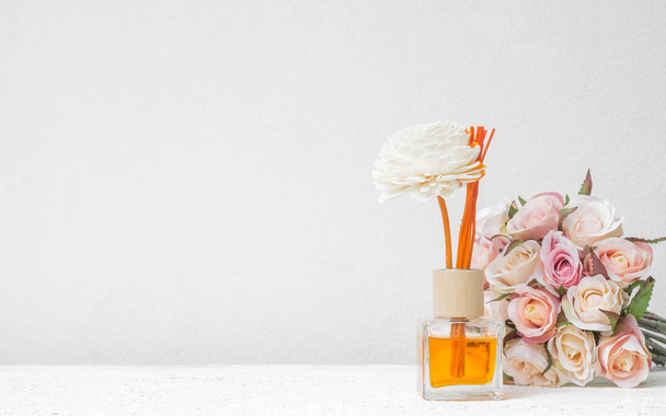 Aromatische reed luchtverfrisser, geur Diffuser Set van fles met aroma stokken (reed diffusoren) met roze bloem op witte muur achtergrond. - Foto, afbeelding