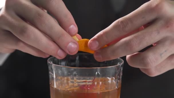 バーテンダーは、アルコール飲料にオレンジの皮を追加します、バーでカクテルを作るバー、アルコール飲料、アルコールのカクテル - 映像、動画