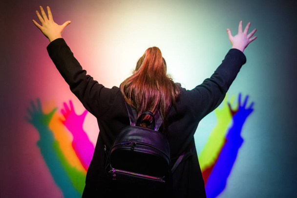 kleurrijke geluk en blije vrouw meisje handen oprijzen in hemel, kleurrijke schaduwen op de muur - Foto, afbeelding