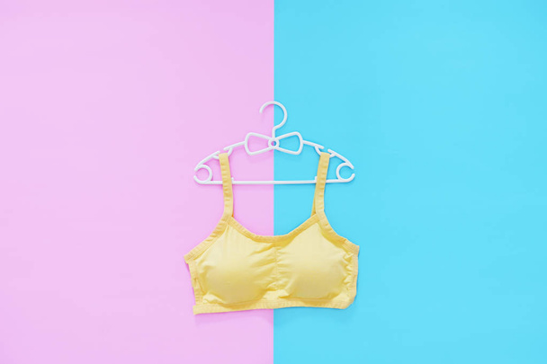 Top View of Sportswear on White Hanger. Women is Yellow Sports Bra Isolated on Pink & Blue Color Pastel. Beautiful Sport Accessories & Fashion, Healthy Lifestyle. Sport Clothes on Two Tone Background. - Zdjęcie, obraz