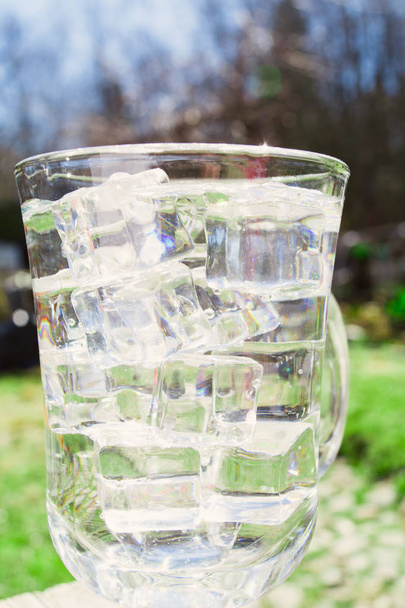 Agua dulce en el vaso con hielo con fondo de jardín, plano vertical
 - Foto, imagen