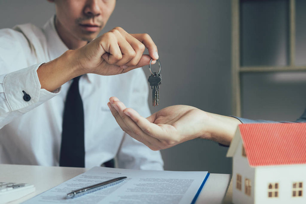 Πωλητής μεσίτες σπιτιών παρέχει το κλειδί για τους νέους ιδιοκτήτες ακινήτων στο γραφείο. - Φωτογραφία, εικόνα