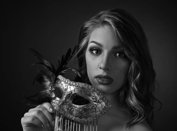 Mujer atractiva con pelo largo rizado sosteniendo en la máscara de carnaval de la mano. Blanco y negro
. - Foto, Imagen