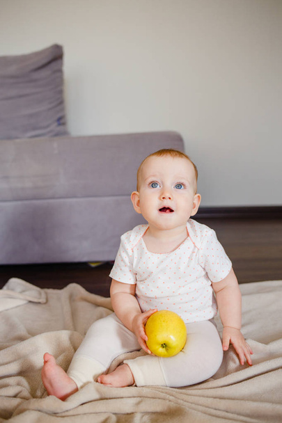 Portrait of a cute little child with one yellow apple, sitting on the floor. Baby girl 9 month old holding a fruit - Foto, imagen