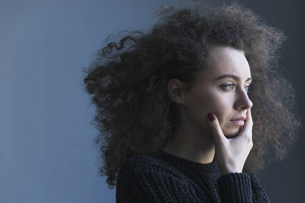 Portrait of stressed young curly woman on dark background - Photo, image