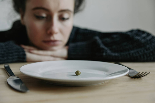 Sad woman looking on pea on white plate - Foto, Bild
