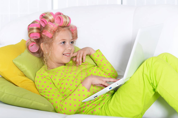 Śliczny mały dziewczyna z różowy lokówki za pomocą laptopa w domu - Zdjęcie, obraz