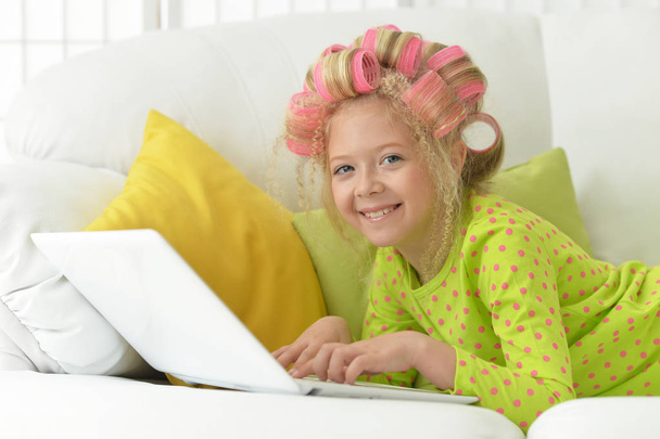 Lovely little girl with pink curlers using laptop  at home - Φωτογραφία, εικόνα