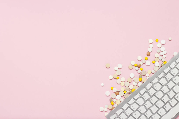 Keyboard and pills on pink background. The concept of ordering and buying medicines, vitamins and pills on the Internet, an online store. Flat lay, top view - Foto, afbeelding