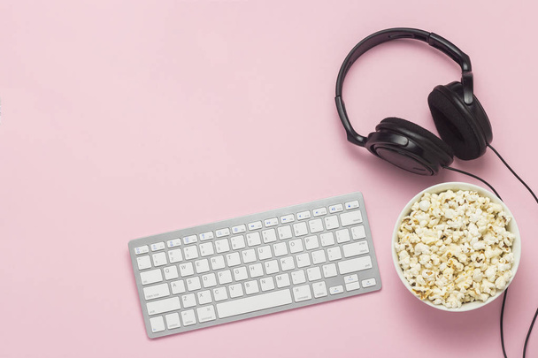 Keyboard, headphones and a bowl of popcorn on a pink background. The concept of watching movies, shows, sports on the PS, games online. Flat lay, top view - Photo, Image