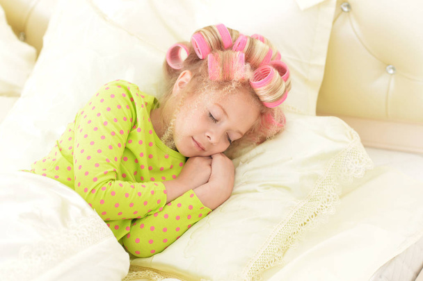 Lovely little girl with pink curlers sleeping in bed at home - Fotografie, Obrázek
